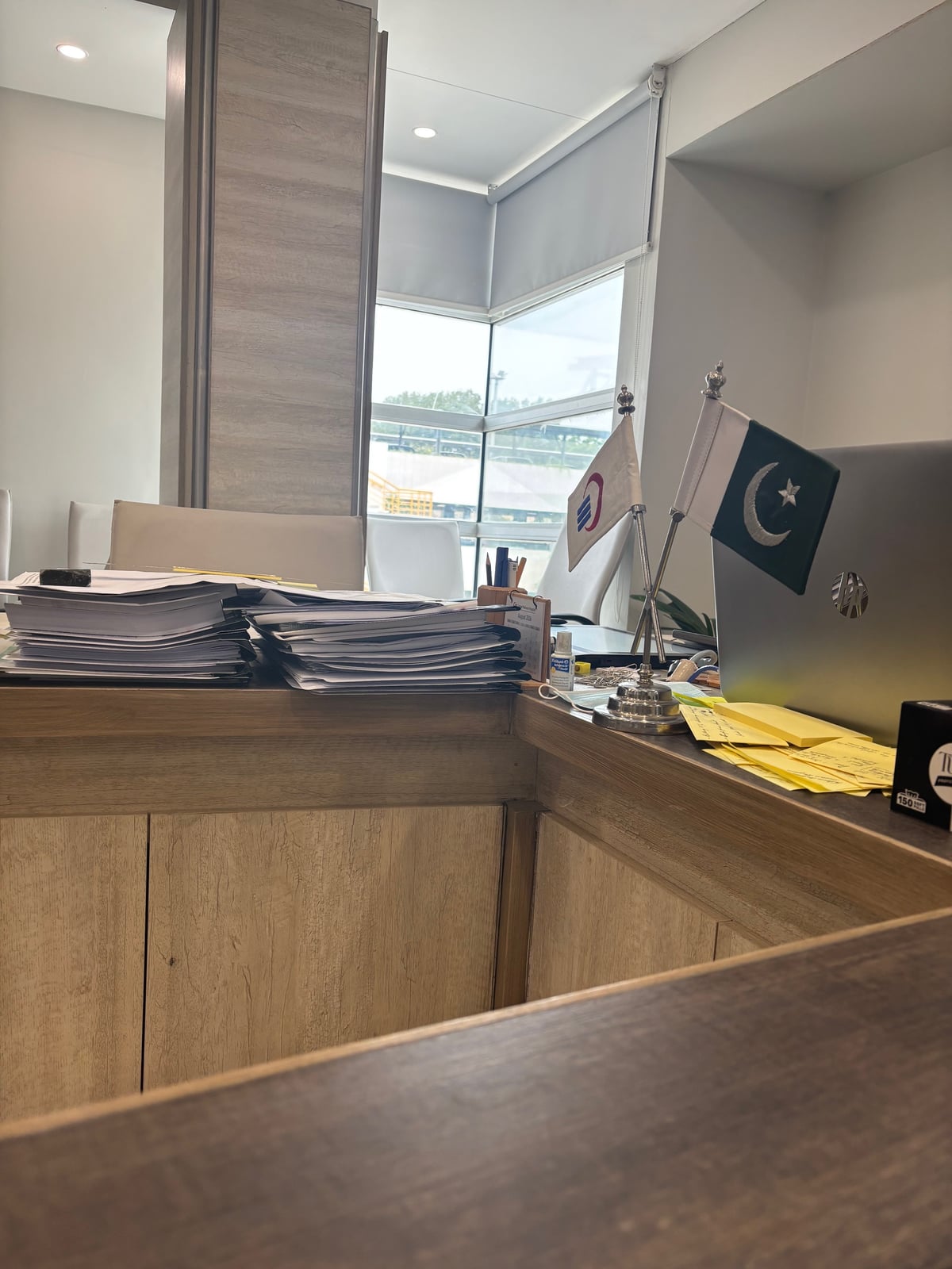 A desk corner at Liaquat National Hospital, with Pakistani and hospital table flags and stacked case files